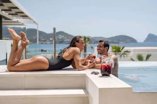 Couple enjoying cocktails by the pool at 7Pines Hotels & Resorts with a stunning ocean view.