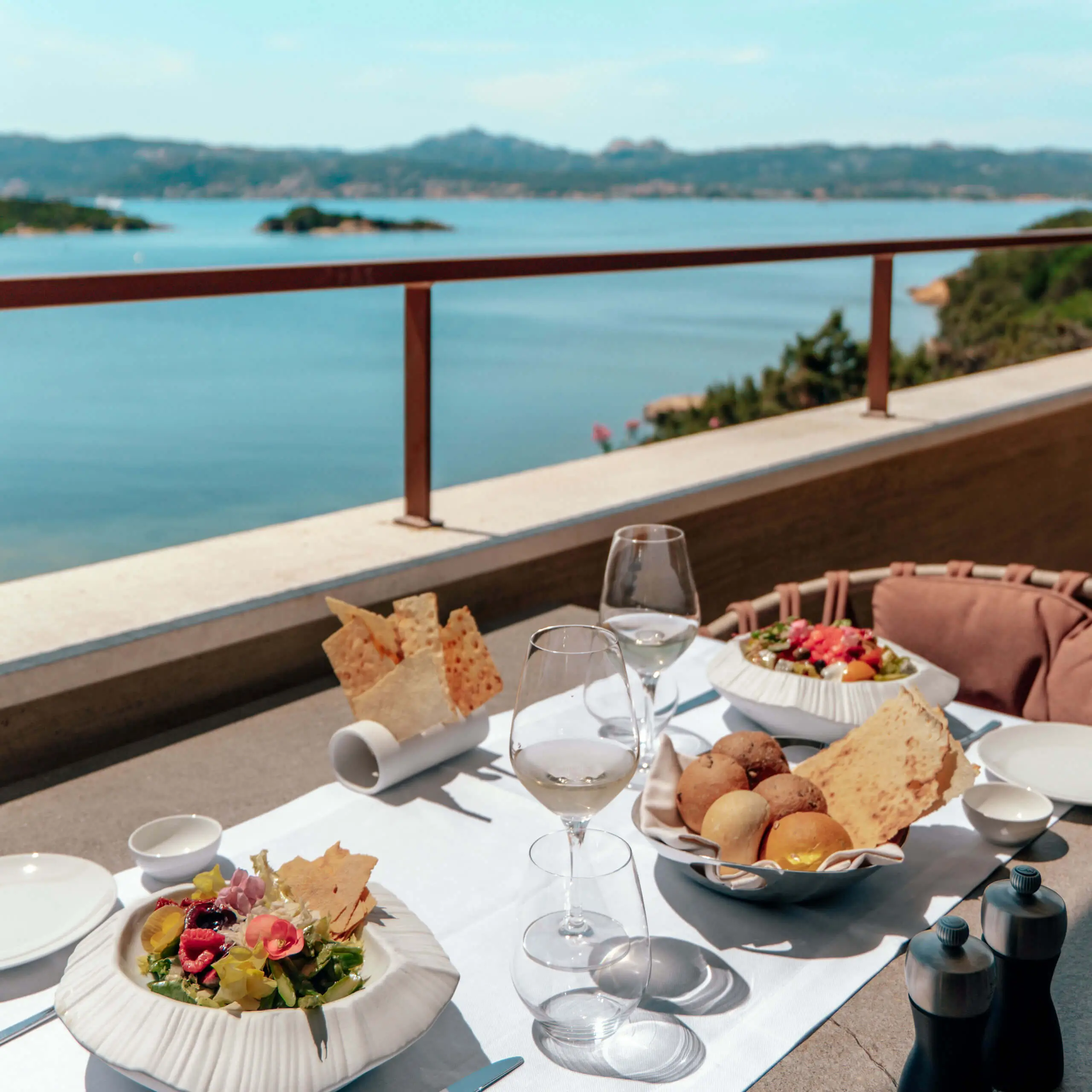 Sea-view dining on the Capogiro terrace at 7Pines, with fresh salads, bread and wine set against the Ibiza coastline.