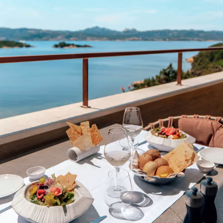 Sea-view dining on the Capogiro terrace at 7Pines, with fresh salads, bread and wine set against the Ibiza coastline.