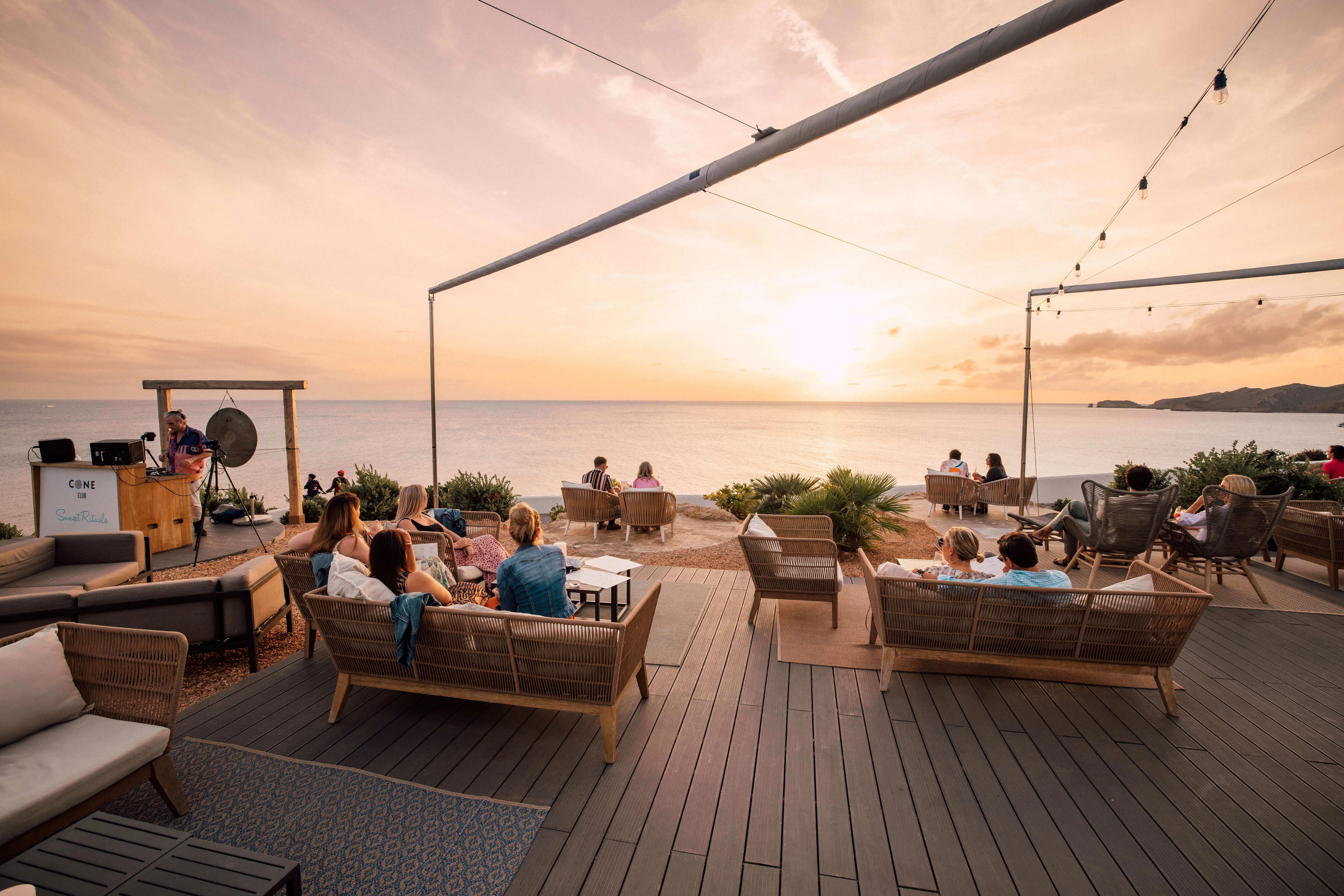 Guests enjoying sunset fine dining on an oceanfront terrace at 7Pines Resort with a live DJ and relaxed lounge seating.