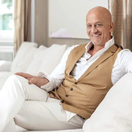 Olaf Kitzig smiling in a stylish vest at a luxury resort interior.