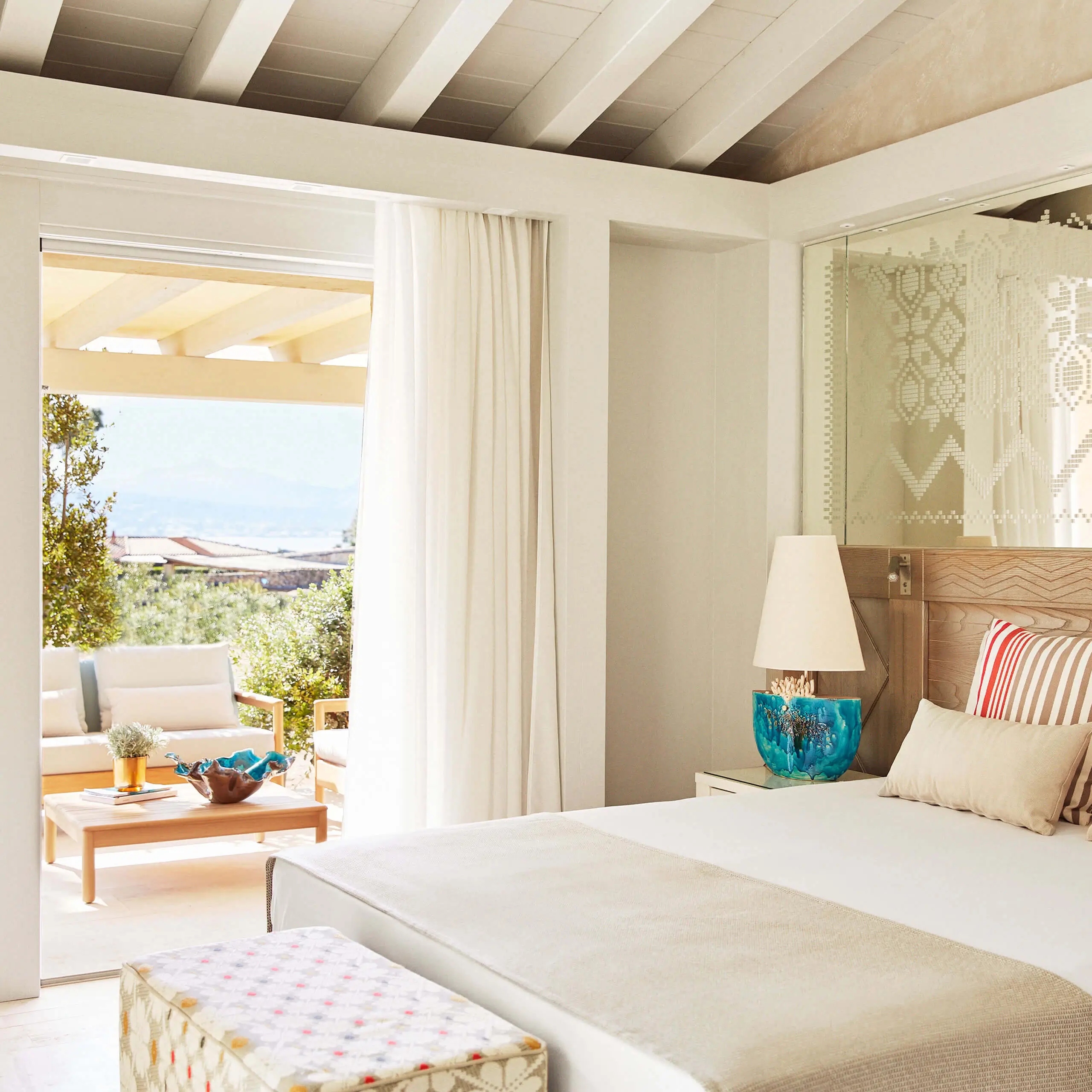 Helles Luxus-Resort-Schlafzimmer bei 7Pines mit weißem Bett, eleganter Einrichtung, Terrassen-Sitzbereich und Meerblick durch weit geöffnete Türen.
