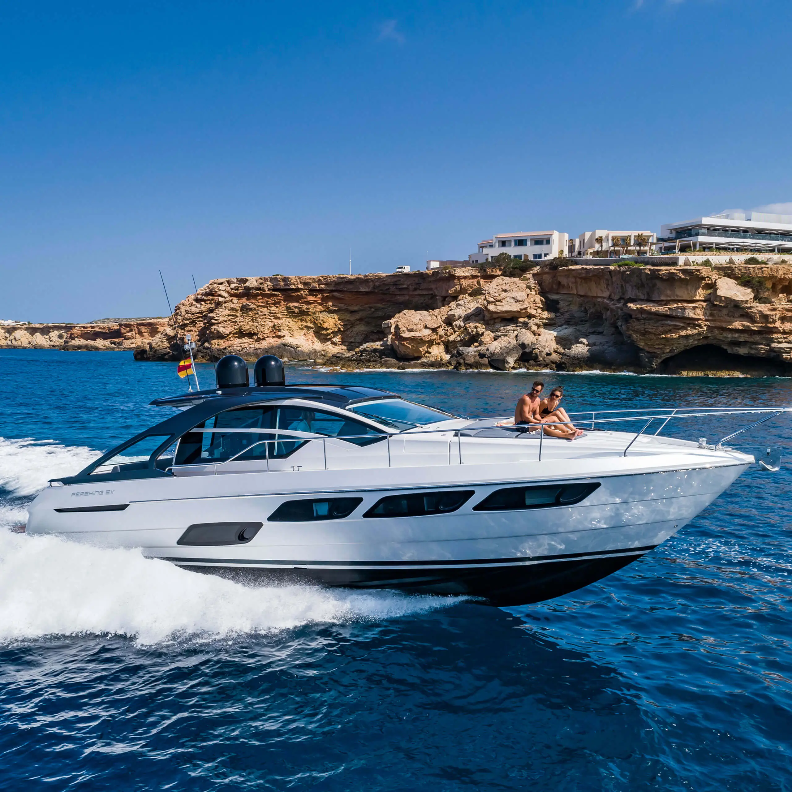 Luxusyacht Pershing 5X fährt entlang der Küste Ibizas mit Gästen an Deck.