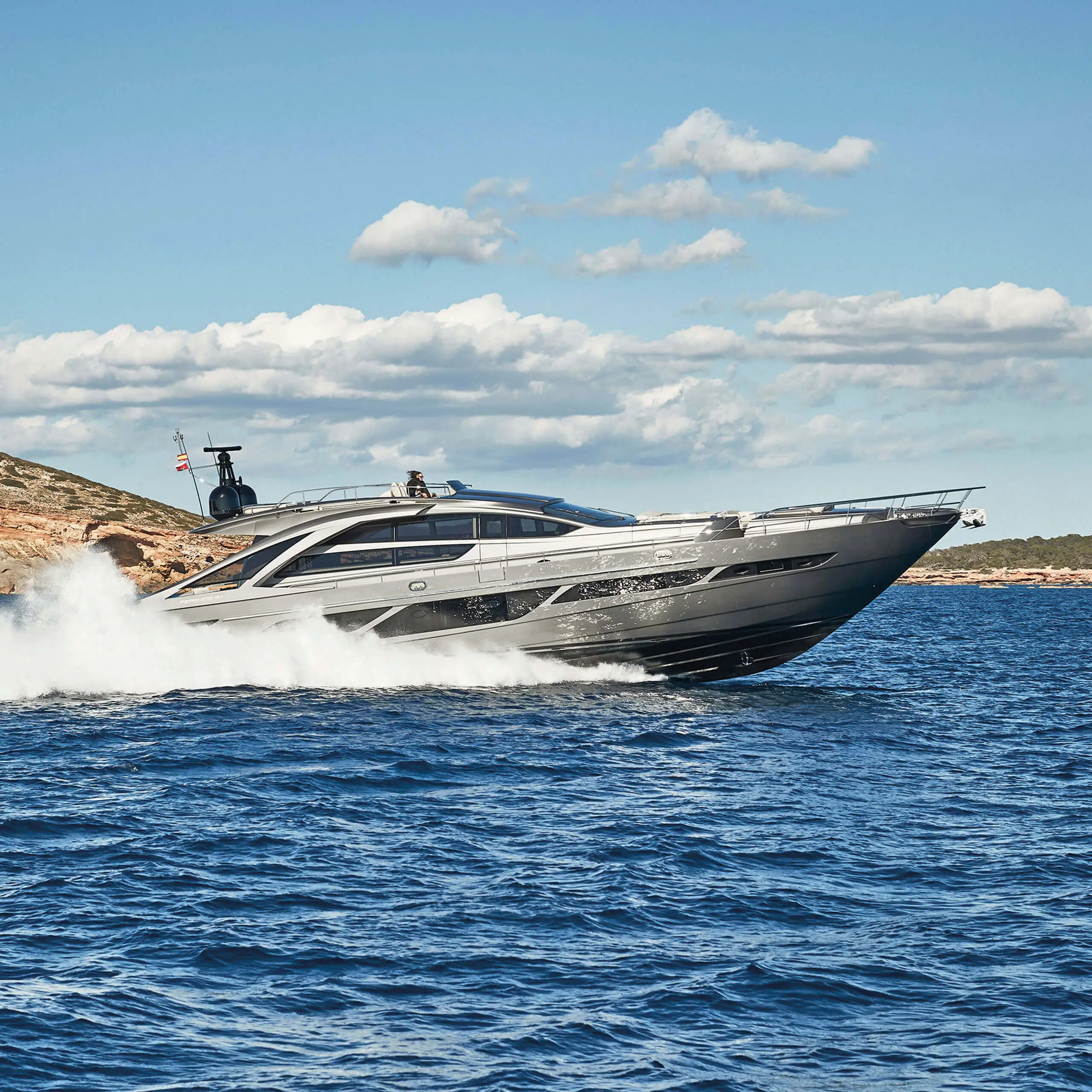 Luxusyacht Pershing 9X fährt an einer felsigen Küste entlang auf klarem blauem Meer im Rahmen eines 7Pines-Yachting-Erlebnisses.