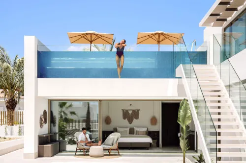 A guest dives into the pool at 7Pines Hotels & Resorts under sun umbrellas.