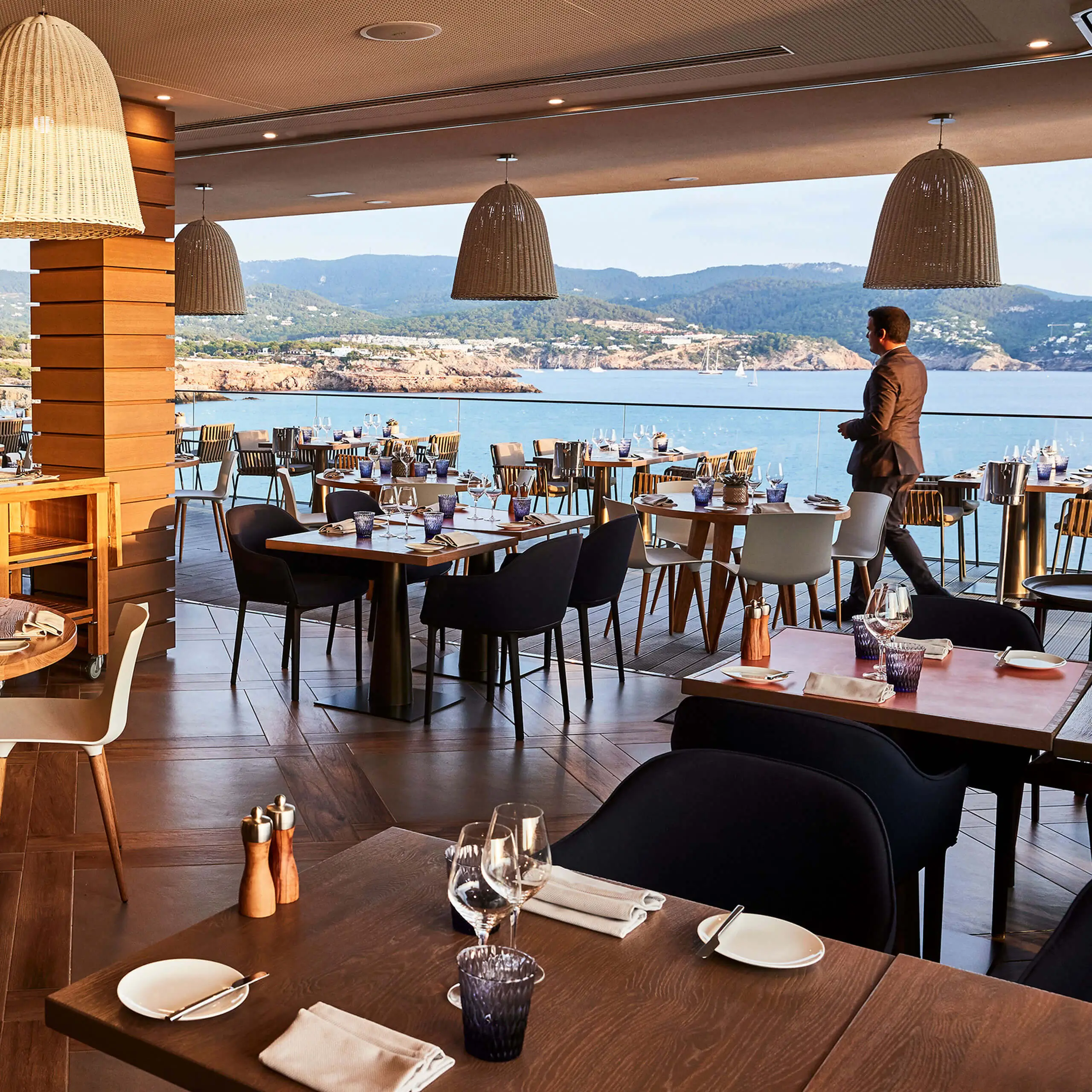 Offene Restaurantterrasse mit Meerblick und gedeckten Tischen über der Bucht.
