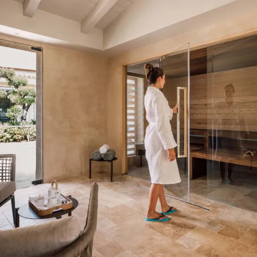 A woman in a robe enters the sauna at 7Pines Hotels & Resorts, embracing wellness and relaxation.