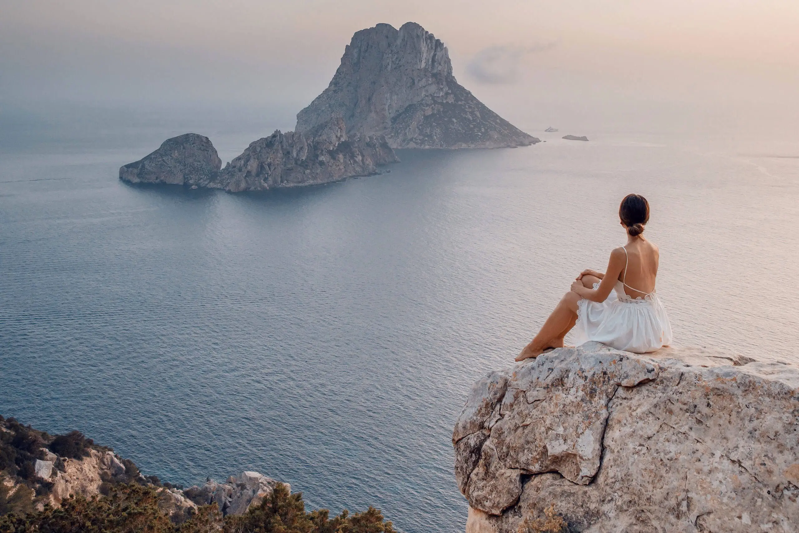Eine Frau genießt die Aussicht auf das Meer von einem Felsen in Ibiza, mit Inseln im Hintergrund.