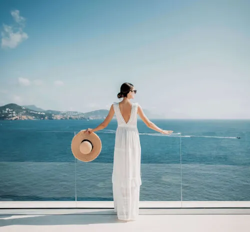 A woman in a white dress enjoys the ocean view from 7Pines Hotels & Resorts.