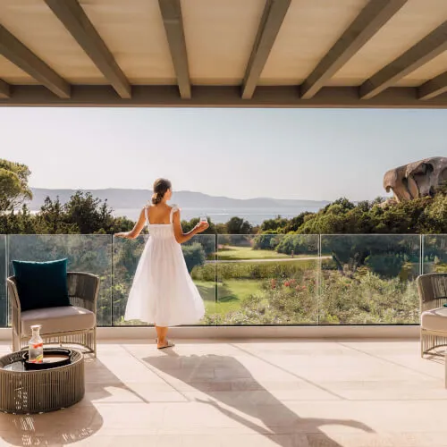 Woman enjoying a drink on the terrace of 7Pines Hotels & Resorts, overlooking lush gardens.