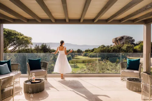 A woman in a white dress on a terrace at 7Pines Hotels & Resorts with a scenic view.