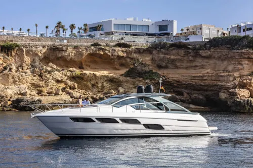 Luxury yacht sailing near cliffs and modern buildings in Sant Josep de sa Talaia.