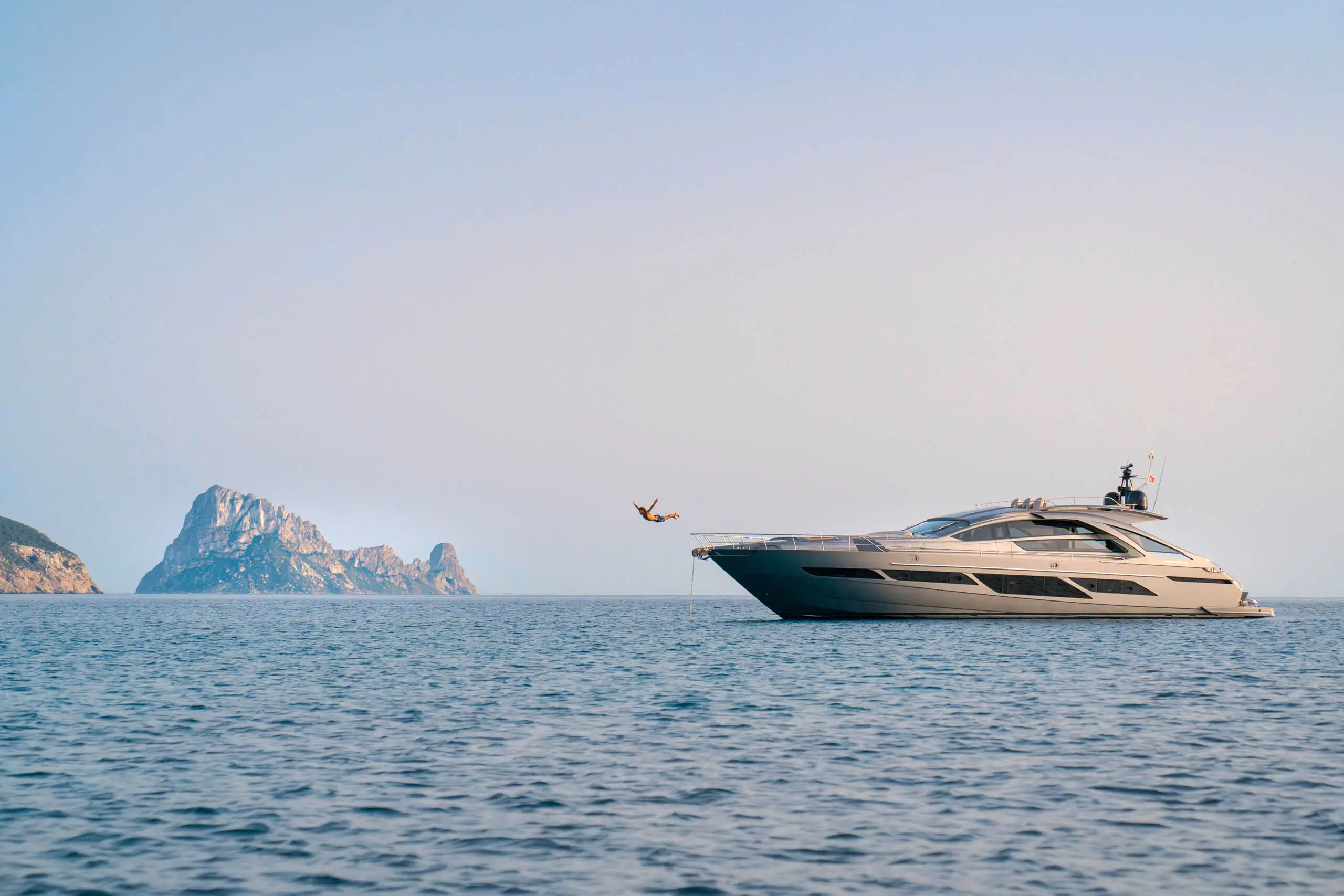 Eine luxuriöse Pershing-Yacht mit einer Person, die in das Meer springt, in der Nähe einer malerischen Felsformation.