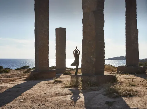 A person practicing yoga in a tranquil setting among stone columns by the beach.